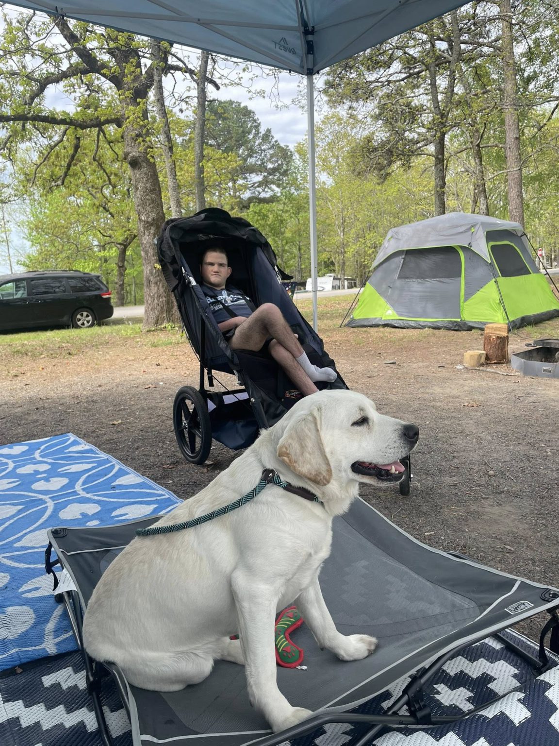 Caden and Shiloh outside at a campsite, Shiloh sitting attentively on his portable mat near Caden
