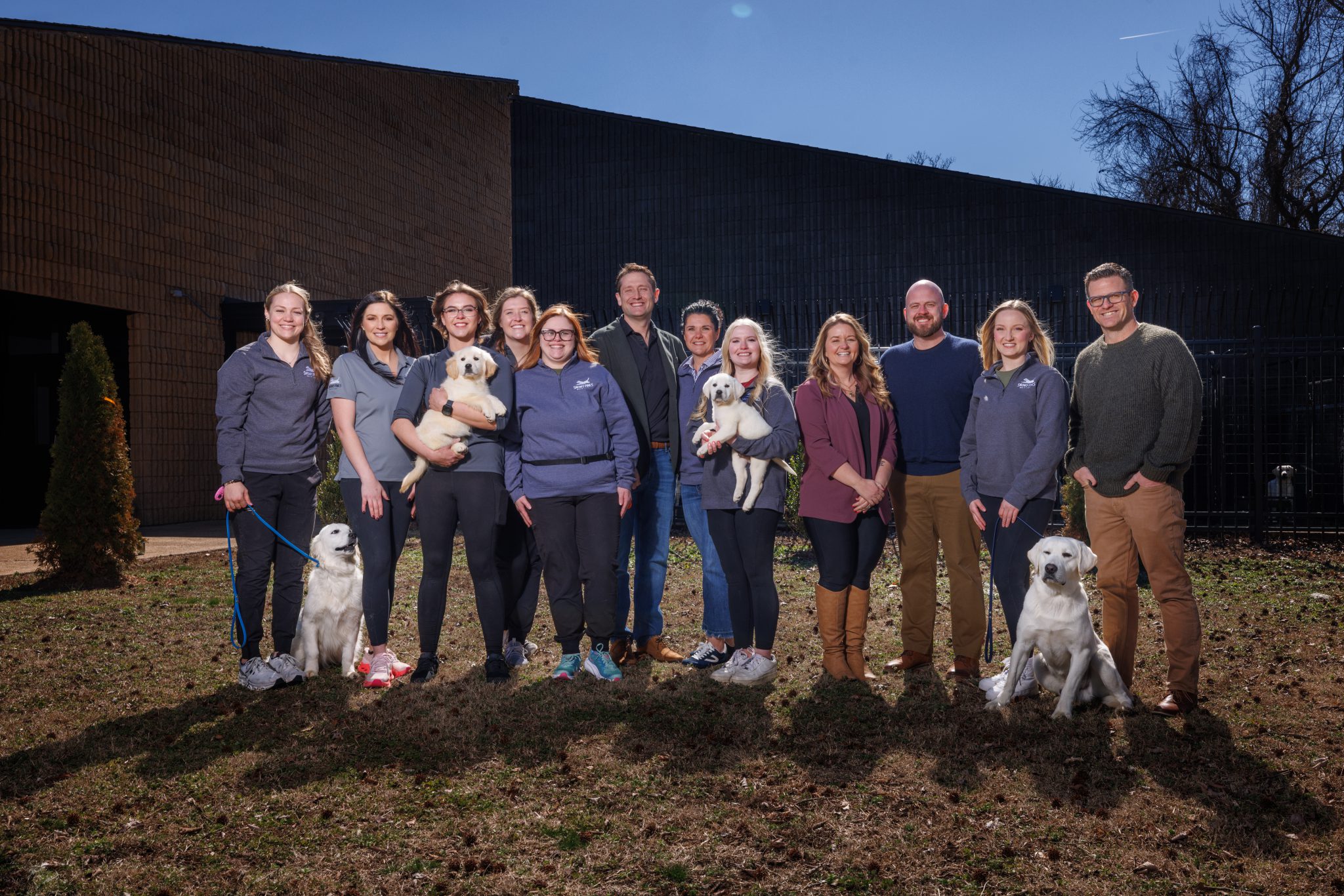 The Snowy Pines / Paws For Purpose team gathered outside the training facility with three of their service dogs